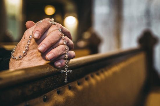 Praying senior hands with rosary in church bench